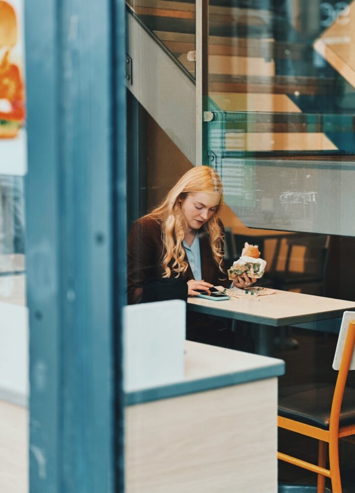 Photo by ONUR KURT Woman eating a sandwich at a cafe table.